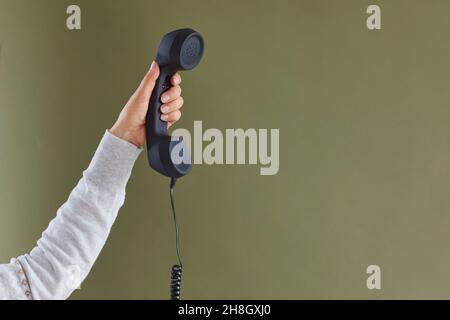 Mano della donna che tiene il ricevitore nero del telefono posteriore sullo sfondo verde dello spazio della copia Foto Stock