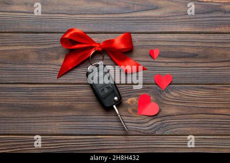 Chiave auto con arco rosso e un cuore su un tavolo colorato. Regalo o regalo per San Valentino o natale, vista dall'alto con spazio per le copie. Foto Stock