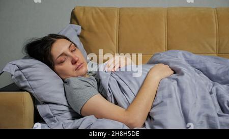 Giovane donna malata si trova sul divano sotto coperta e tosse Foto Stock