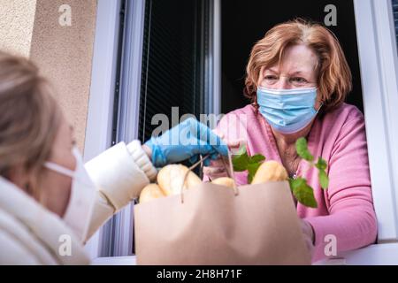 Donna che consegna generi alimentari e cibo alla madre anziana. Divaricamento sociale dovuto blocco pandemico del coronavirus Foto Stock