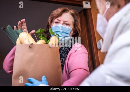 Volontario indossare maschera ffp2 durante la consegna di generi alimentari alla donna anziana. Sostenere la comunità locale degli anziani con il blocco covid-19. Aiuto di mano con il negozio Foto Stock