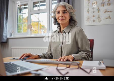 Ritratto del GP femminile maturo alla scrivania in Ufficio Medici Foto Stock