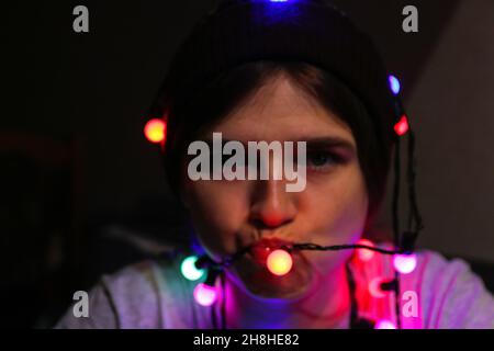 Defocus ritratto di Natale. Primo piano folle felice giovane donna celebrare natale. I giovani si divertono durante le vacanze invernali. Donna avvolta in c Foto Stock