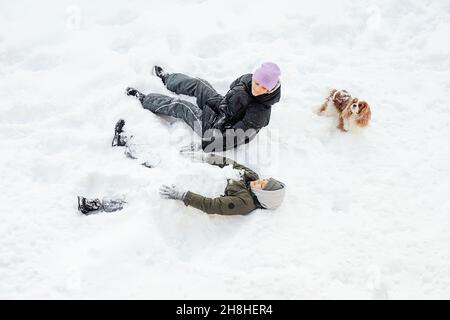 Ragazzo e ragazza, adolescenti. Fratello, sorella indulgere in, sdraiato nella neve, in giornata nevosa con il cane. In inverno, i fiocchi di neve volano in diverse direzioni di happin Foto Stock