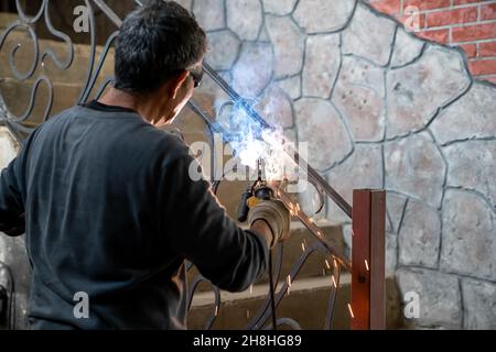 Lavori di saldatura su metallo in casa privata. L'uomo in occhiali di sicurezza è metallo di saldatura della griglia della scala. Primo piano. Foto Stock