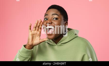 Gioiosa Signora Africana urlando la mano di tenuta vicino alla bocca, sfondo rosa Foto Stock