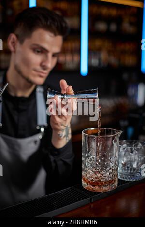 Barman in grembiule aggiunge l'ingrediente al vetro Foto Stock