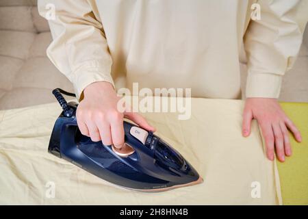 Una mano donna con un ferro blu scuro Philips Azur e un asse da stiro, primo piano - Mosca, Russia, 01 novembre 2021 Foto Stock