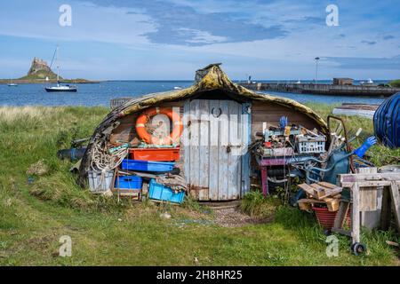 Imbarcazione capovolta utilizzata come capanna sulla spiaggia con vista distante del Castello di Lindisfarne sulla costa del Northumberland d'Inghilterra, Regno Unito Foto Stock