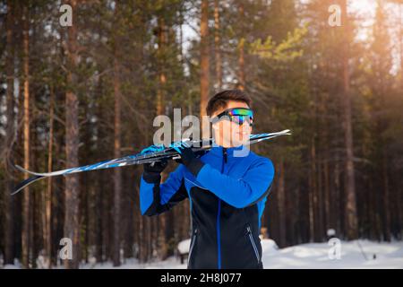 Ritratto di pilota sciatore maschio con sci di fondo sullo sfondo della foresta invernale. Foto Stock