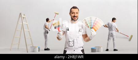 Casa pittore che tiene una tavolozza di colori e un pennello e altri pittori che dipinge un muro isolato su sfondo bianco Foto Stock