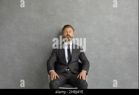 Uomo d'affari serio e pensivo seduto su una sedia e guardando in su ponderando le nuove idee. Foto Stock