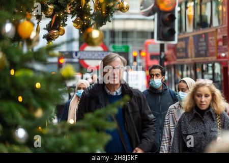 Londra, Regno Unito. 30 novembre 2021. La gente passa gli alberi di Natale fuori da Harvey Nichols a Knightsbridge il primo giorno in cui le coperture di faccia sono di nuovo richieste nei negozi seguendo le nuove misure del governo britannico per cercare di frenare la diffusione del coronavirus dopo il rilevamento della variante di Omicron. Credit: Stephen Chung / Alamy Live News Foto Stock