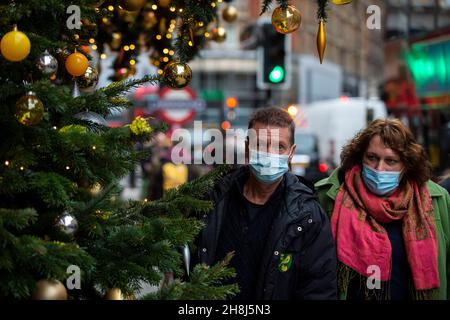 Londra, Regno Unito. 30 novembre 2021. Una coppia passa gli alberi di Natale al di fuori di Harvey Nichols a Knightsbridge il primo giorno in cui le coperture del viso sono di nuovo richieste nei negozi seguendo le nuove misure del governo britannico per cercare di frenare la diffusione del coronavirus in seguito al rilevamento della variante Omicron. Credit: Stephen Chung / Alamy Live News Foto Stock