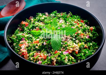 Autentico Tabouleh libanese guarnito con foglie di menta: Una grande ciotola di insalata di prezzemolo con grano di bulgur, pomodori e cipolle Foto Stock