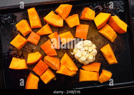 Zucca cotta cruda e bulbo all'aglio su una tovaglietta: Vista dall'alto della zucca e dell'aglio insaporiti nell'olio d'oliva per la tostatura Foto Stock