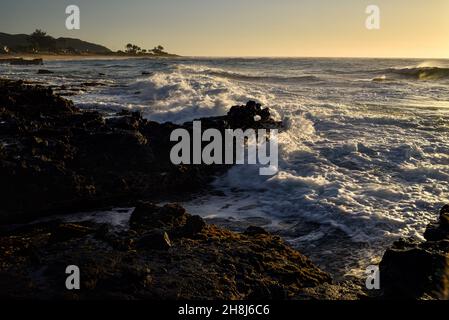 Sunrise mentre il surf si schianta e si gira intorno alle rocce di lava vulcanica al Sandy Beach Park, Oahu orientale, Hawaii Kai, Hawaii, USA Foto Stock