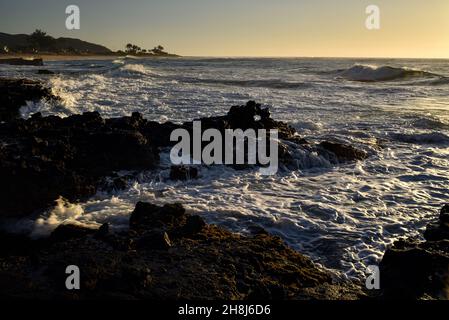 Sunrise mentre il surf si schianta e si gira intorno alle rocce di lava vulcanica al Sandy Beach Park, Oahu orientale, Hawaii Kai, Hawaii, USA Foto Stock