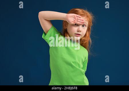 primo piano di foto di piccola ragazza emotiva rossa in posa prima della fotocamera su sfondo blu Foto Stock