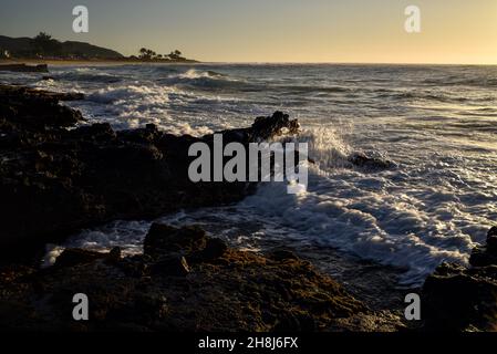 Sunrise mentre il surf si schianta e si gira intorno alle rocce di lava vulcanica al Sandy Beach Park, Oahu orientale, Hawaii Kai, Hawaii, USA Foto Stock