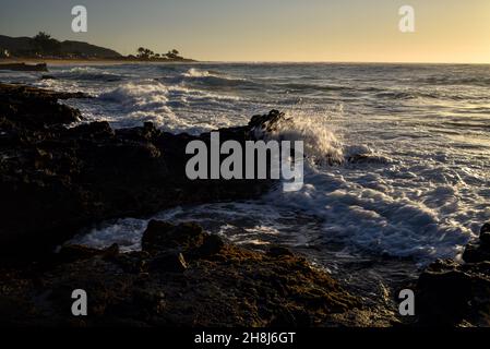 Sunrise mentre il surf si schianta e si gira intorno alle rocce di lava vulcanica al Sandy Beach Park, Oahu orientale, Hawaii Kai, Hawaii, USA Foto Stock