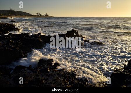 Sunrise mentre il surf si schianta e si gira intorno alle rocce di lava vulcanica al Sandy Beach Park, Oahu orientale, Hawaii Kai, Hawaii, USA Foto Stock