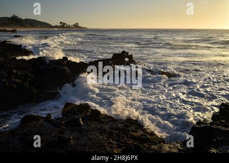 Sunrise mentre il surf si schianta e si gira intorno alle rocce di lava vulcanica al Sandy Beach Park, Oahu orientale, Hawaii Kai, Hawaii, USA Foto Stock