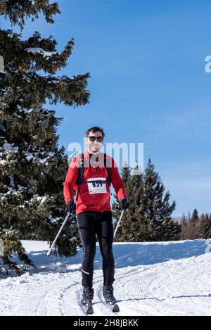 Uno sciatore di fondo maschile in una maglia rossa di pullover compete nel Chama Chile Ski Classic in una giornata intensa con cieli blu. Foto Stock