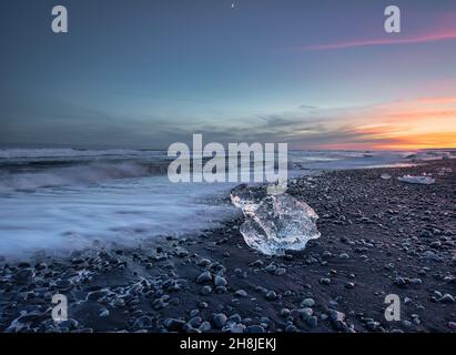 Un pezzo unico di ghiaccio sulla famosa spiaggia nera di Jokulsarlon, Islanda, durante il tramonto. Foto Stock
