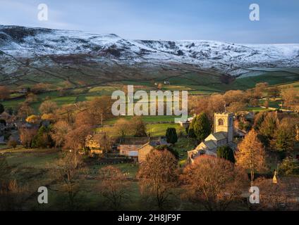 Un breve lampo di luce all'alba illumina la Chiesa di San Wilfrid nel grazioso villaggio di Burnsall con le colline dietro coperte di prima nevicata. Foto Stock