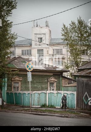 15 maggio 2016, Russia, Tomsk, vecchia donna wlaks su strada sullo sfondo di vecchi edifici sovietici architettura Foto Stock