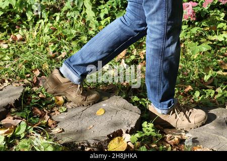 Un uomo cammina lungo un sentiero forestale. Gambe in pantaloni e stivali. Foto Stock