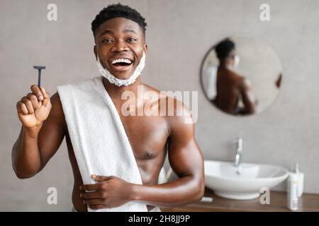 Il Razor di sicurezza dell'uomo nero eccitato in stanza da bagno Foto Stock