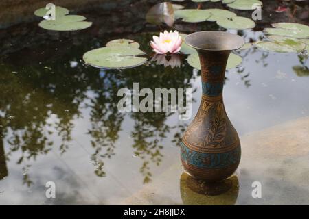 Antico vaso di rame indiano sul lago con giglio Foto Stock