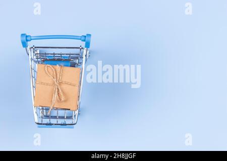 Vista dall'alto al mini carrello con piccolo kraft carta regalo presente scatola su sfondo blu chiaro. E-commerce, concetto di shopping online Foto Stock