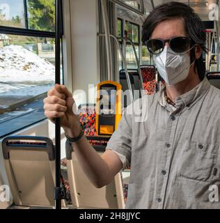 Uomo con capelli neri con respiratore e camicia grigia in streetcar in inverno giorno di sole Foto Stock