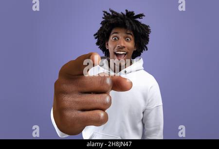 Funky teen ragazzo nero puntando indice dito alla fotocamera, che fa grande HO SCELTO voi gesto su sfondo viola studio Foto Stock