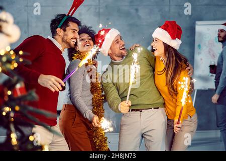 Festa di Capodanno in azienda. Un gruppo di colleghi multiculturali sta in piedi nella sala di consiglio alla vigilia di Capodanno e tenendo fuochi d'artificio e celebrità a mano Foto Stock