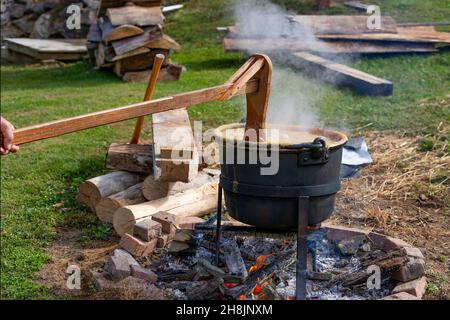 Cucinare il burro di mela il vecchio modo di moda in un bollitore nero su una buca di fuoco aperta. Foto Stock