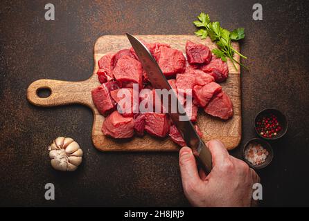 Taglio a mano maschile a cubetti di carne di manzo crudo su tavola di legno Foto Stock