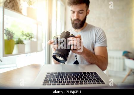 Giovane fotografo che regola le impostazioni sulla sua fotocamera. Preparazione del ritocco delle foto sul computer. Foto Stock