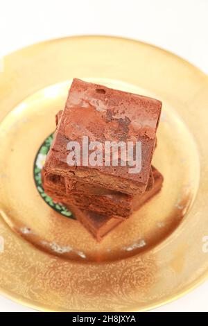 Tre Brownies accatastati su piatto d'oro, bontà al cioccolato. Fotografia verticale chiara e luminosa scattata in un ambiente di studio. Foto Stock