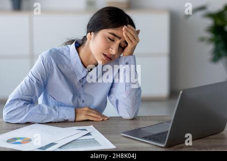 Triste stanco giovane dipendente indiano signora preme mano a testa sul posto di lavoro con il laptop in ufficio o a casa Foto Stock
