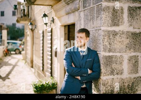 Sorridente uomo barbuto dai capelli rossi appoggiato al muro di una vecchia casa di pietra Foto Stock