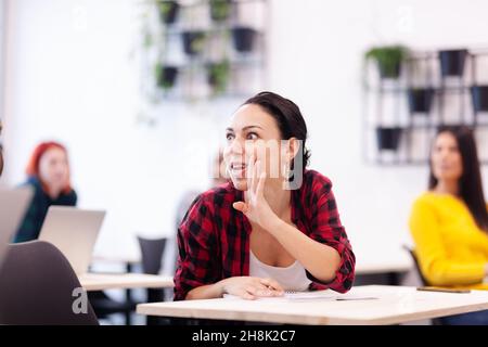 Studenti multietnici che ascoltano un docente in un'aula. Giovane donna intelligente che sussurra ai colleghi durante la lezione. Foto Stock