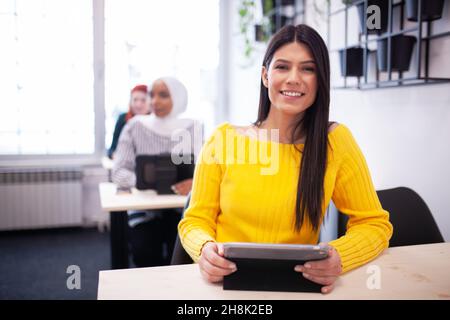 Studenti che ascoltano un docente in un'aula. Giovane donna intelligente sorridente e in posa per la fotocamera. Foto Stock