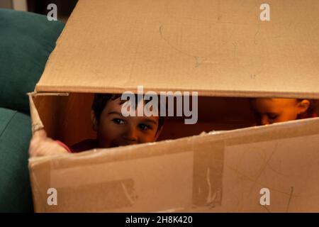 Bambino che gioca e guarda attraverso la crepa di una scatola di cartone Foto Stock