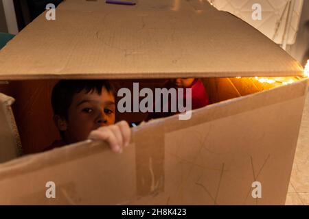 Bambino che gioca e guarda attraverso la crepa di una scatola di cartone Foto Stock