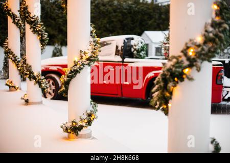 Idea decorazione portico di Natale. Ingresso casa con porta rossa decorata  per le vacanze. Corona rossa e verde di rami di abete e luci sulla ringhiera.  Vigilia di Natale a casa Foto