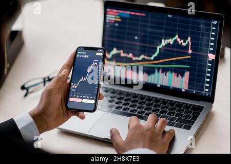 Primo piano dello schermo di un computer portatile e di un cellulare con diagrammi. Crypto trader Investor broker che utilizza smartphone e laptop per l'analisi del mercato finanziario della criptovaluta, l'acquisto o la vendita di criptovaluta Foto Stock